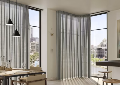 Elegant residential dining area with large corner windows dressed in floor-to-ceiling sheer grey wave curtains, offering a city skyline view.